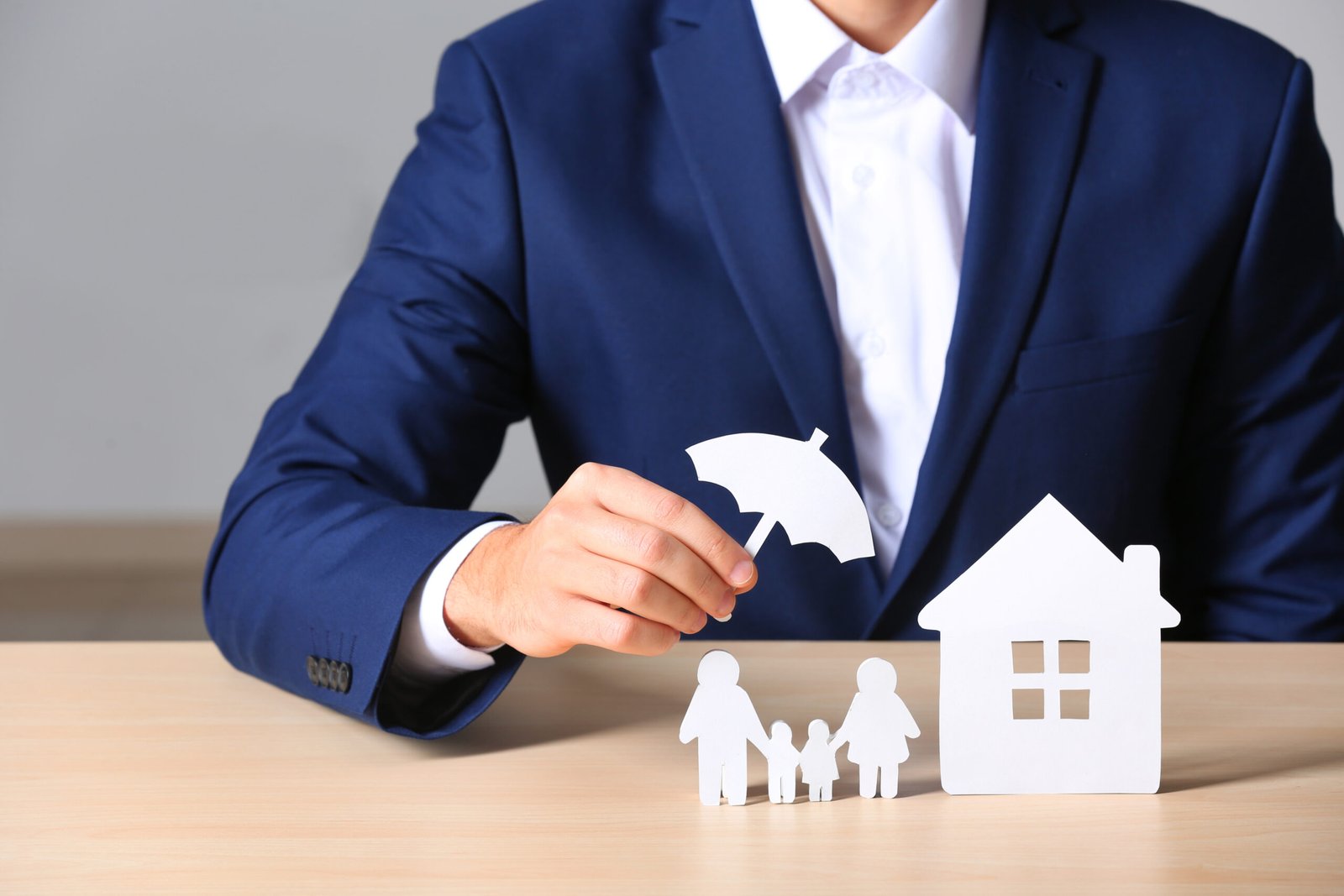 Male insurance agent covering paper family and home with umbrella cutout at table, closeup